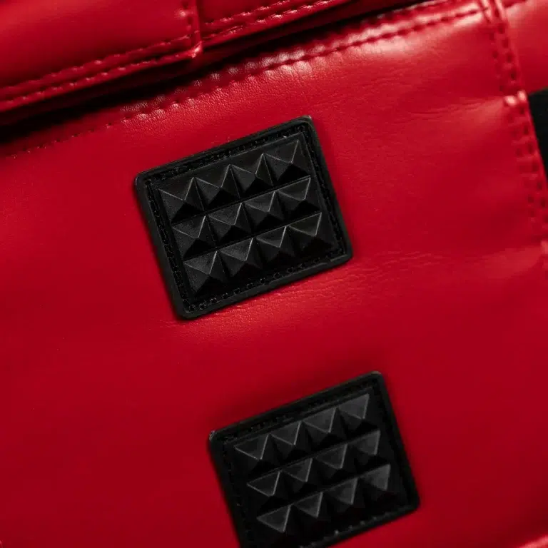 Close-up of red leather bag featuring two black rectangular studs with pyramid patterns. ขายราคาพิเศษ