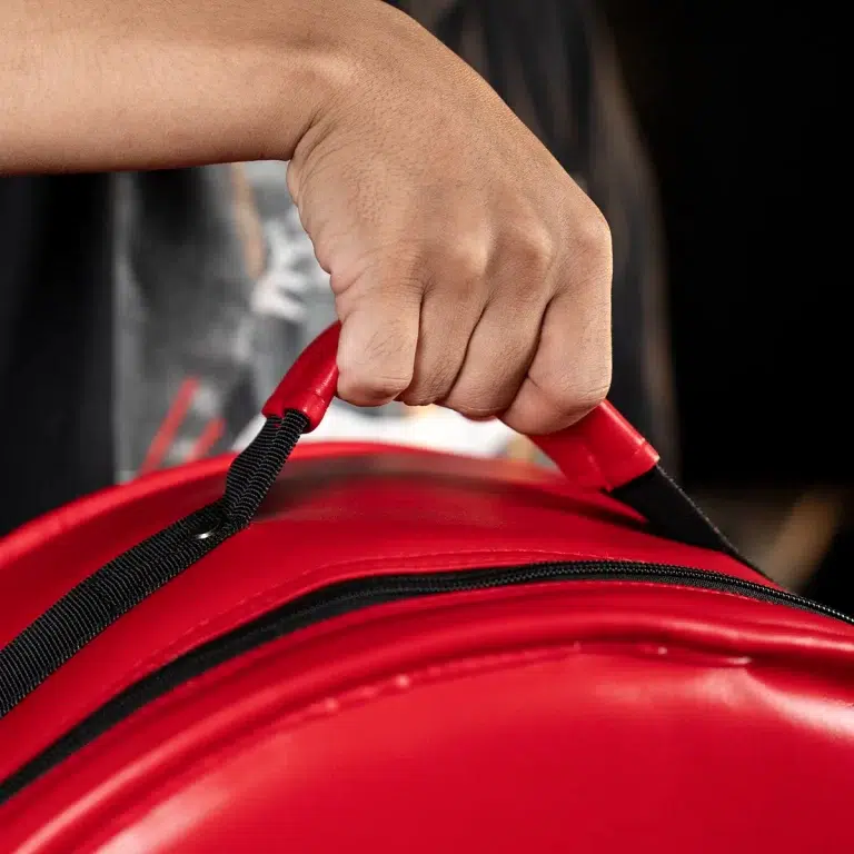 Person's hand grips the red handle of a shiny red bag with a black zipper visible nearby. ขายราคาพิเศษ