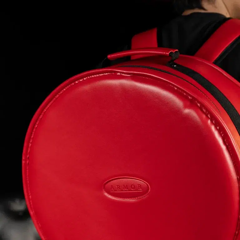 Close-up of a round red backpack with a black zipper and embossed ARMOR logo. ขายราคาพิเศษ