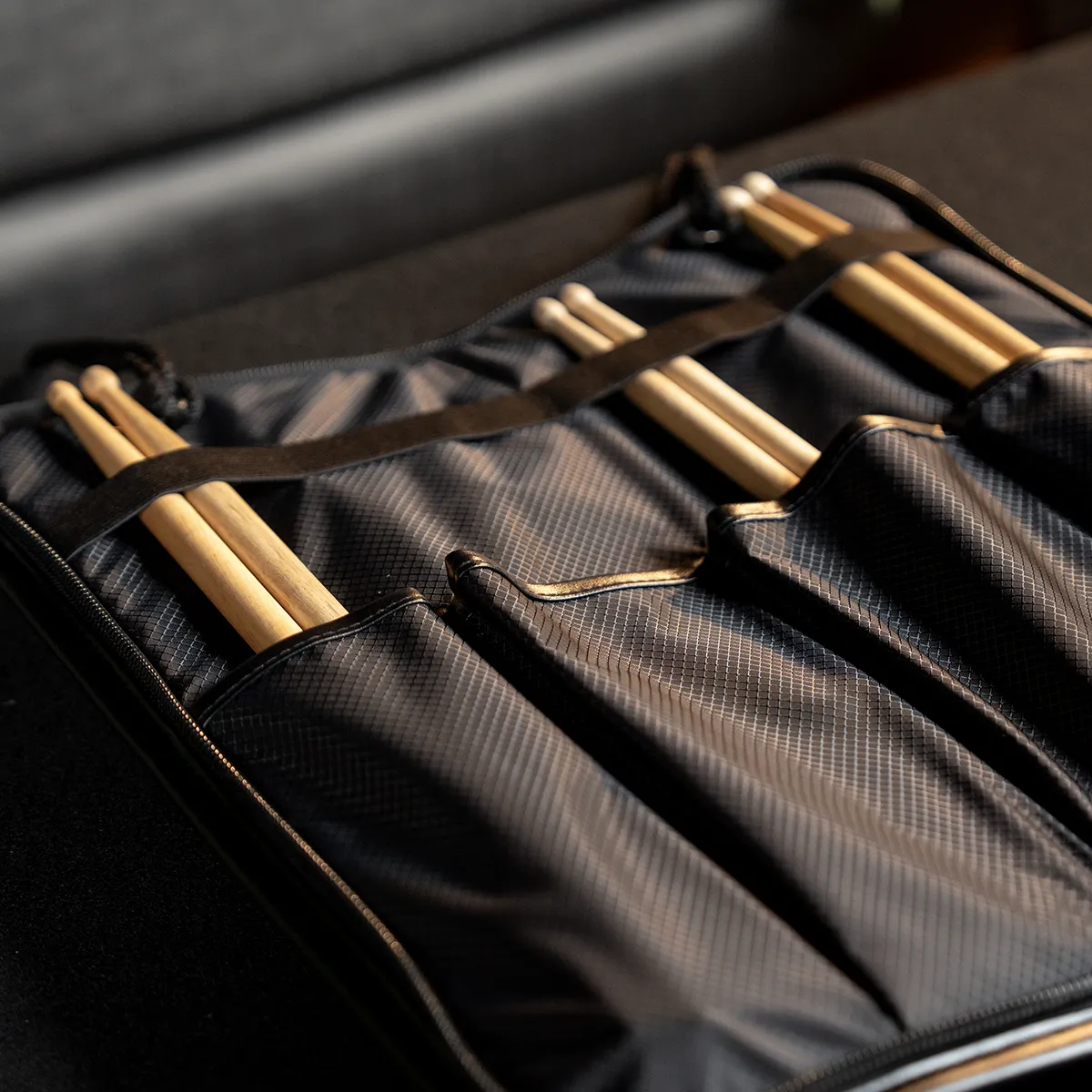 Open black roll-up bag with beige wooden knitting needles secured in slots in a dark fabric case.