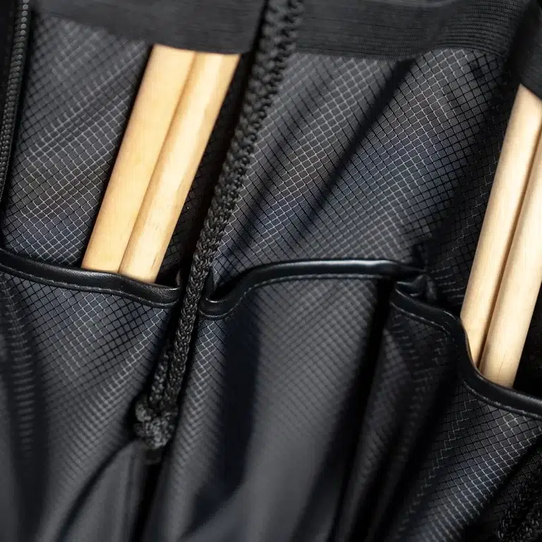 Close-up of a black textured backpack pocket with light wooden drumsticks tucked inside. ขายราคาพิเศษ
