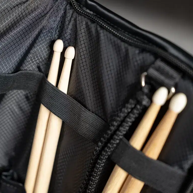 Wooden drumsticks tucked into a black backpack with elastic straps and zippers in a close-up view. ขายราคาพิเศษ