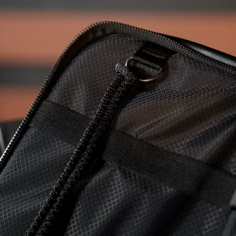 Close-up of a black bag showing a zipper, a fabric loop, a metal D-ring, and a braided strap attachment. ขายราคาพิเศษ