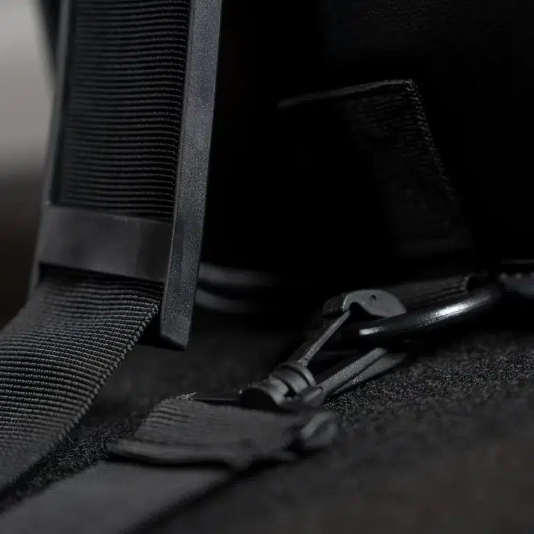 Close-up of black backpack straps and zipper hardware on dark fabric, showing stitching and plastic buckles. ขายราคาพิเศษ
