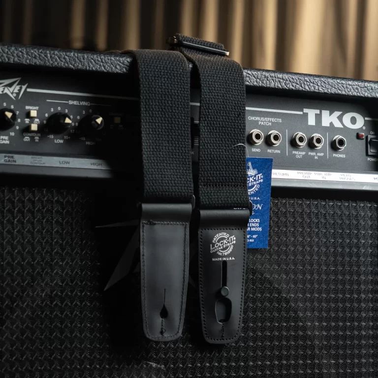 Close-up of two black leather strap buttons and a thick fabric guitar strap attached to a guitar amplifier, with 'TKO' visible on the amp panel. ขายราคาพิเศษ