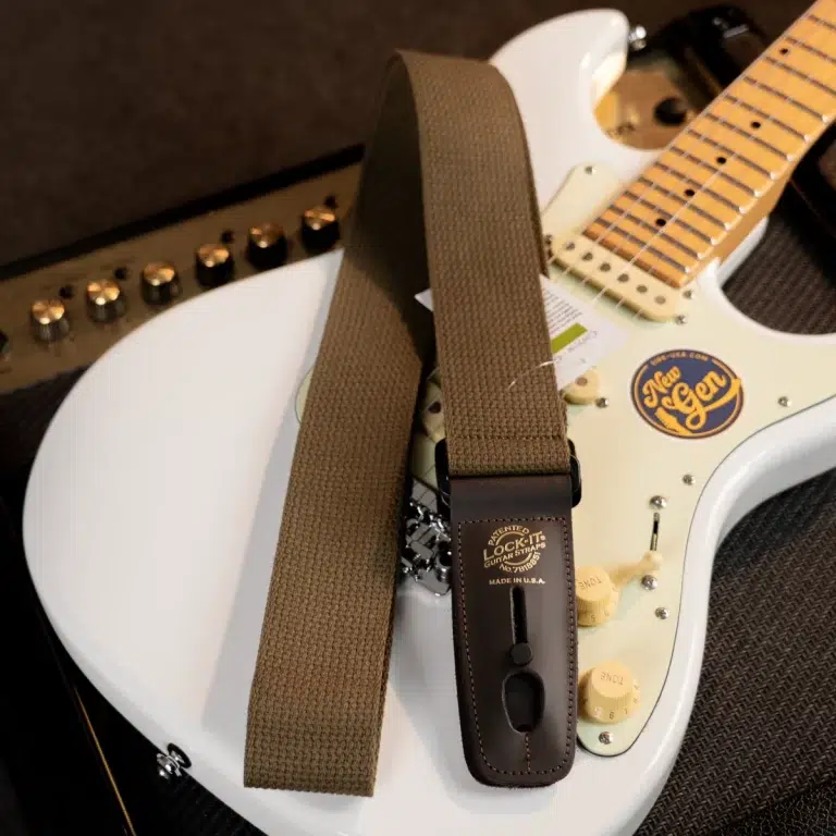White electric guitar with a brown woven strap draped over it, leather strap end reads 'LOCK-IT' ขายราคาพิเศษ