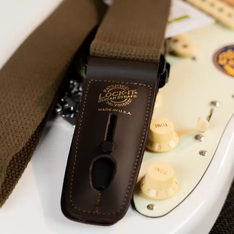 Close-up of a brown leather Lock-It guitar strap attached to a white electric guitar with cream control knobs visible nearby. ขายราคาพิเศษ