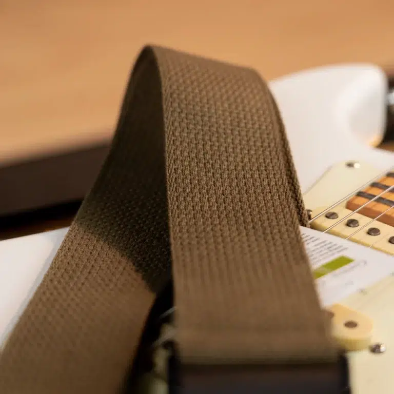 Close-up of a brown woven guitar strap resting on a white electric guitar, with strings and control area visible in the background. ขายราคาพิเศษ