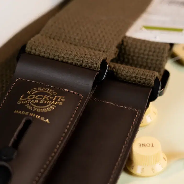Close-up of a brown leather-ended guitar strap with stitched edges and a gold-embossed brand logo reading 'Lock It Guitar Straps'. ขายราคาพิเศษ