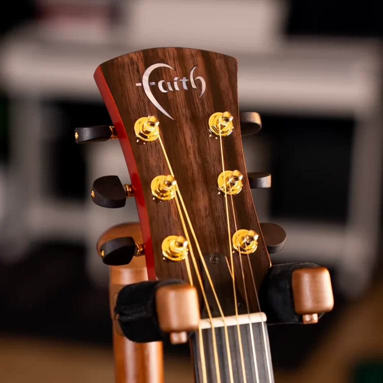 Close-up of a Faith acoustic guitar headstock with gold tuners and strings, mounted on a stand. ขายราคาพิเศษ