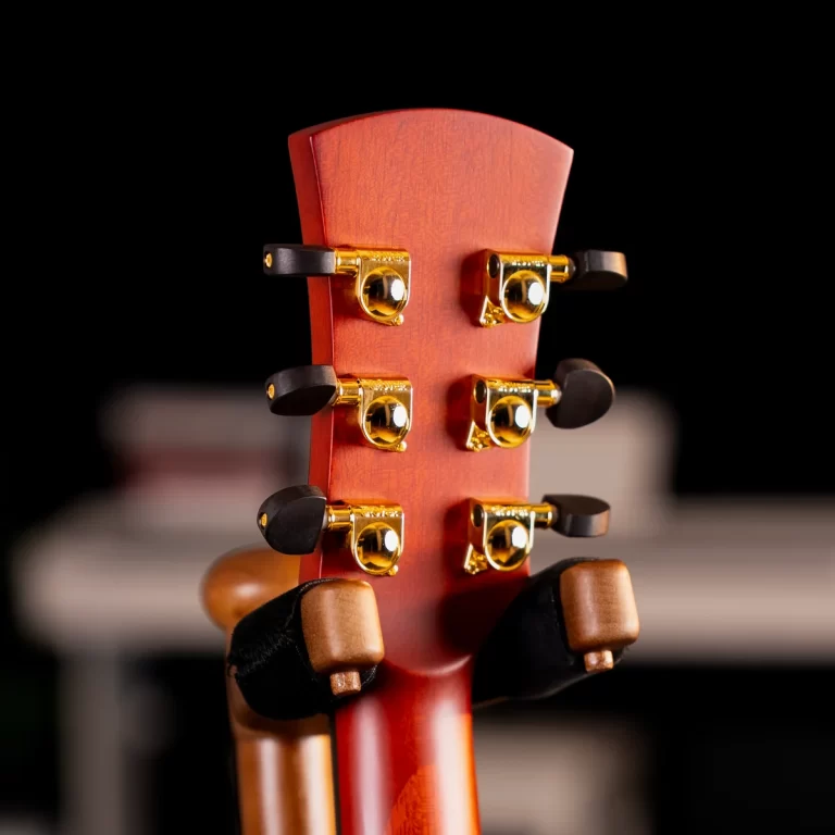 Close-up of a guitar headstock with six gold tuning pegs on a reddish wood neck, set against a dark background. ขายราคาพิเศษ