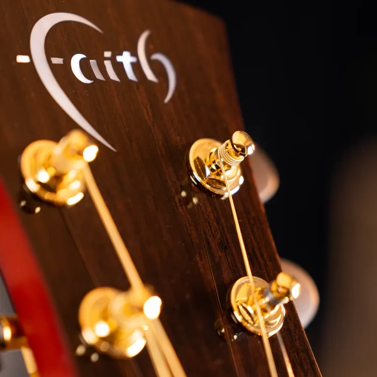 Close-up of a guitar headstock with gold tuning pegs and strings, a partial brand logo visible on dark wood. ขายราคาพิเศษ