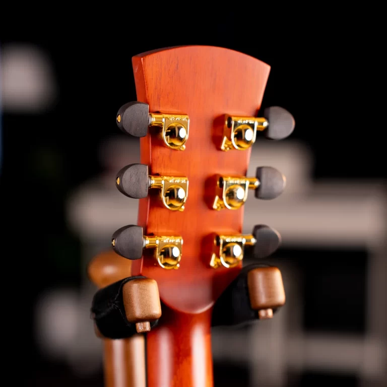 Close-up of a guitar headstock with gold tuning pegs on a reddish wooden neck against a dark background. ขายราคาพิเศษ