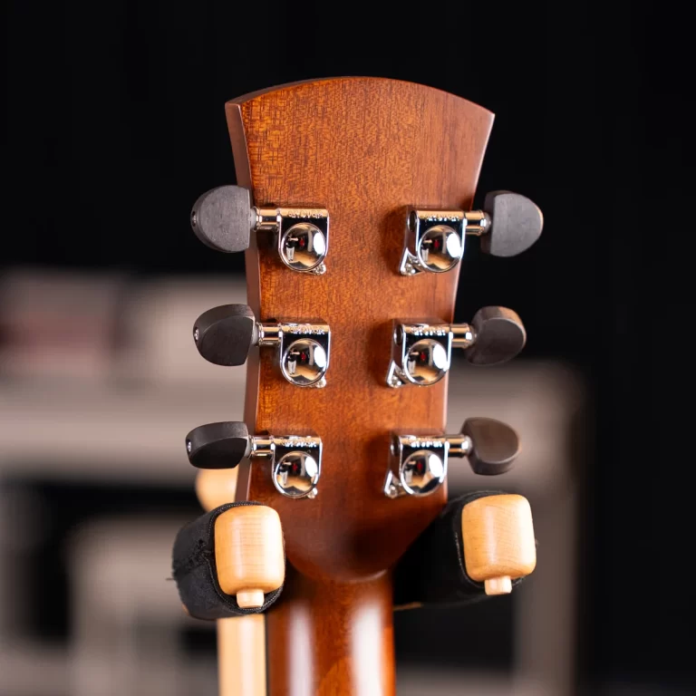 Close-up of a wooden guitar headstock with chrome tuners and black tuning pegs on a dark background. ขายราคาพิเศษ