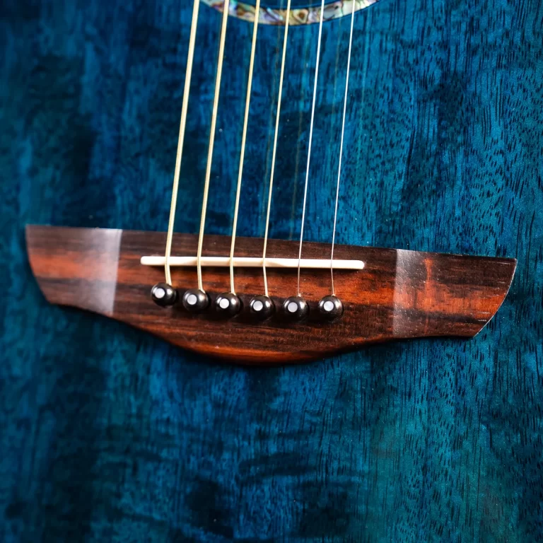 Close-up of a guitar bridge with six strings on a dark wood body against a blue textured background. ขายราคาพิเศษ