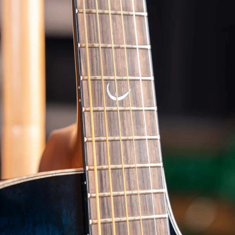 Close-up of a guitar neck showing frets, strings, and a white crescent inlay on the fretboard ขายราคาพิเศษ