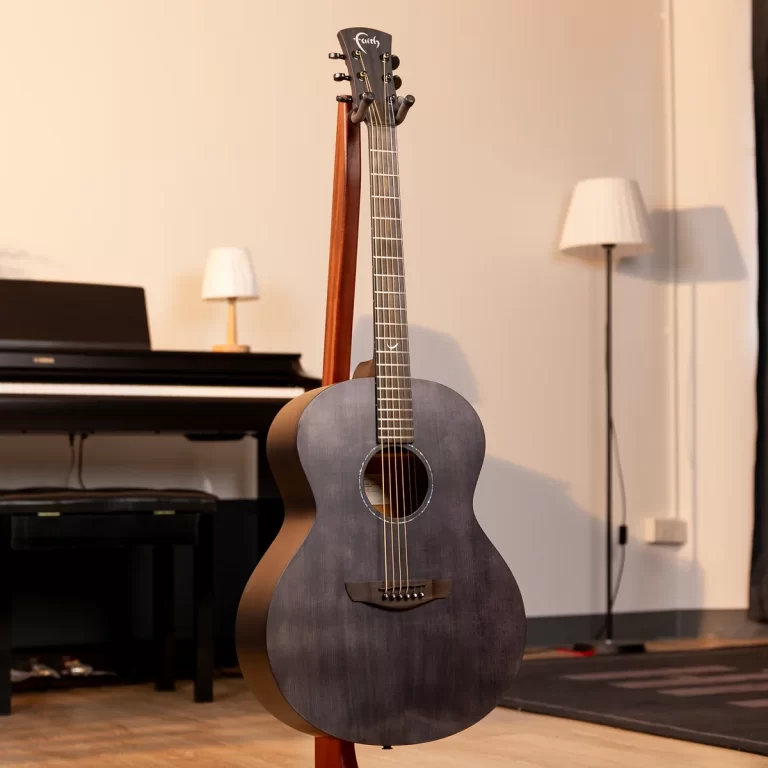 Dark gray acoustic guitar on a stand in a room with a black piano and white lampshade in the background. ขายราคาพิเศษ