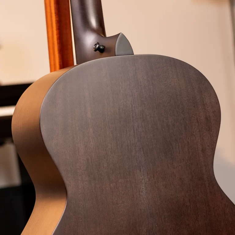 Close-up of the back of a dark wooden acoustic guitar showing the curved body and neck joint at the top edge of the guitar body. ขายราคาพิเศษ