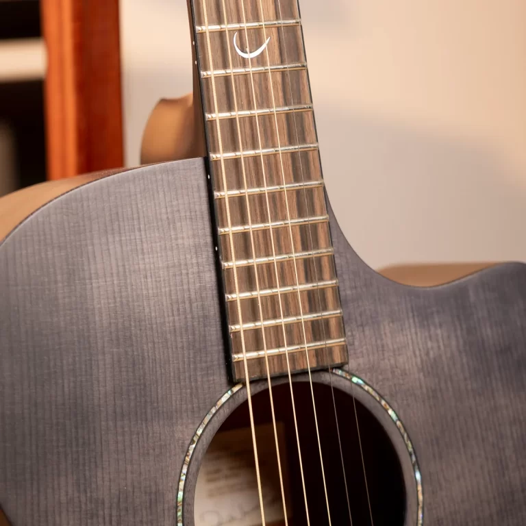 Close-up of a gray acoustic guitar neck and fretboard with six strings running along the frets, body and soundhole visible at the bottom. ขายราคาพิเศษ