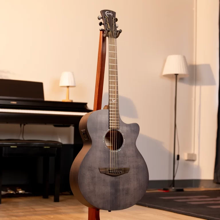 Gray acoustic guitar on a stand in a cozy music room with a piano in the background and a floor lamp nearby ขายราคาพิเศษ