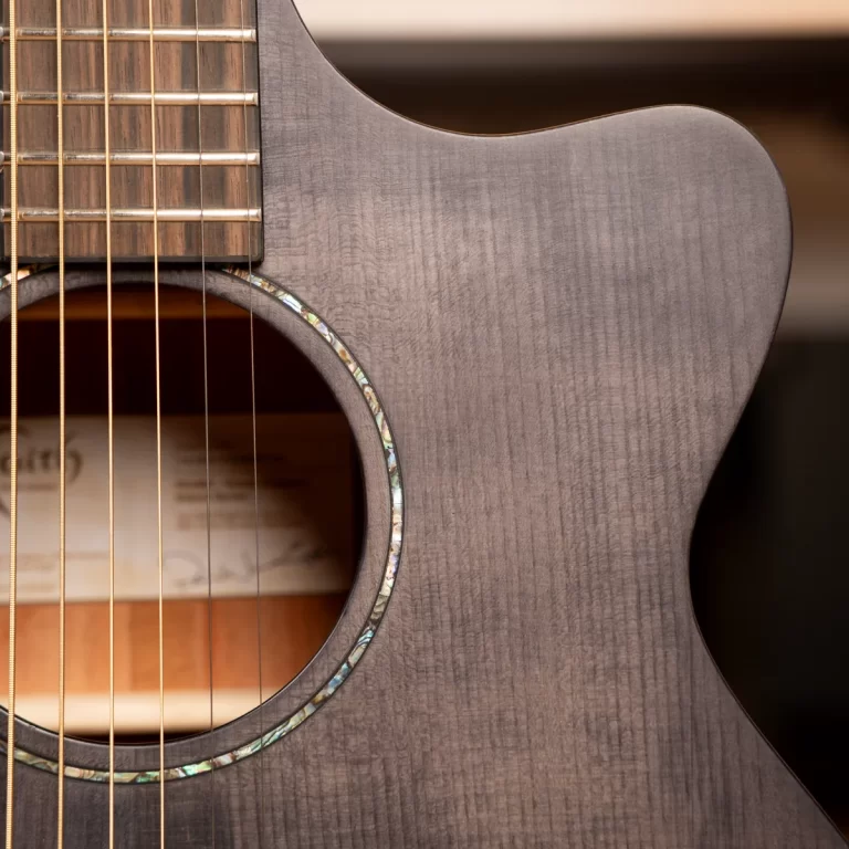 Close-up of an acoustic guitar body showing the soundhole, rosette, and strings over a gray wood grain finish ขายราคาพิเศษ