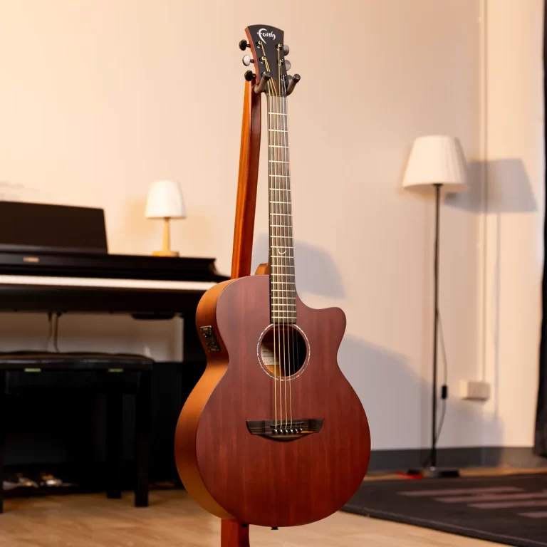 Wooden acoustic guitar on a stand in a cozy living space with a piano and lamps in the background ขายราคาพิเศษ