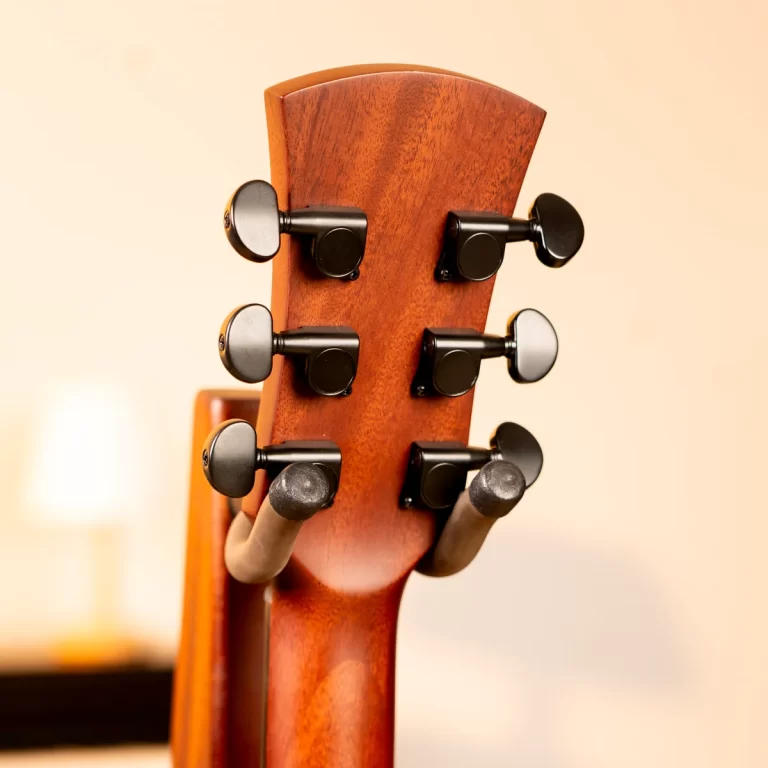 Close-up of a wooden guitar headstock with six black tuning pegs against a soft, warm background. ขายราคาพิเศษ