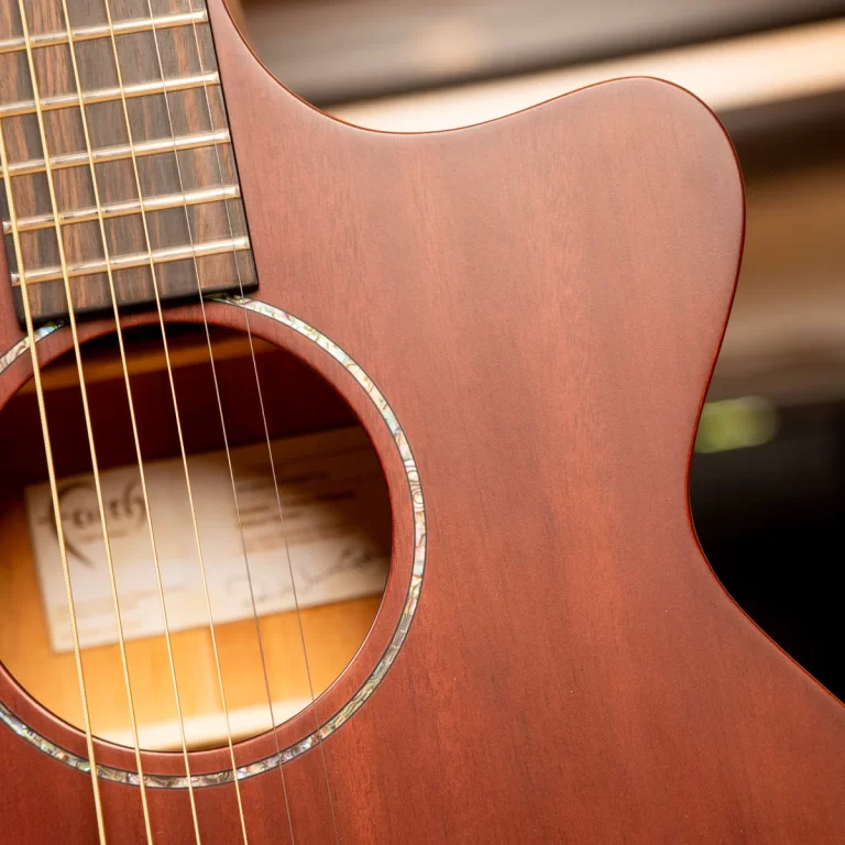 Close-up of an acoustic guitar body with strings over the soundhole and wood grain visible ขายราคาพิเศษ