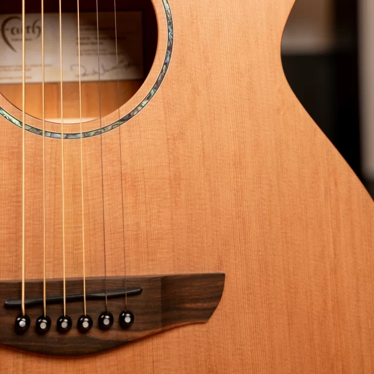 Close-up of an acoustic guitar body: six strings over the dark wooden bridge with bridge pins, partly showing the sound hole and wood grain. ขายราคาพิเศษ
