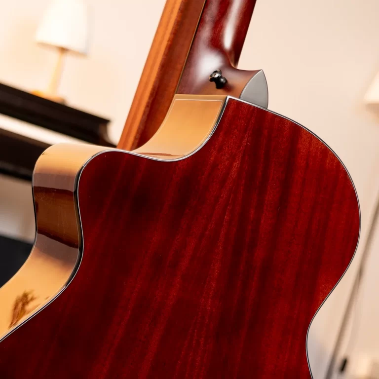 Close-up of a glossy reddish-brown acoustic guitar body with a cutaway and binding, in a warm indoor setting. ขายราคาพิเศษ