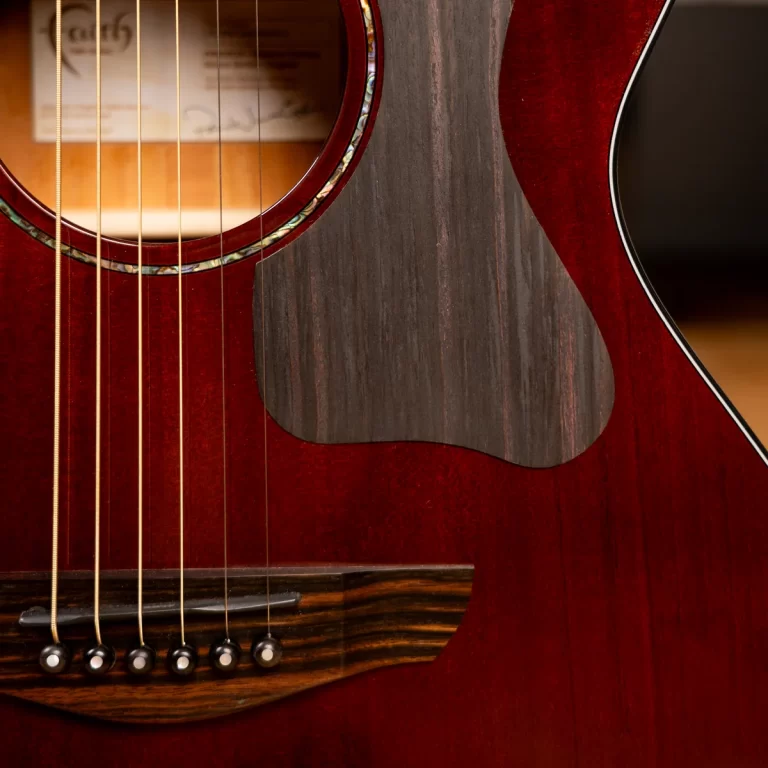Close-up of a red acoustic guitar showing strings over the bridge and soundhole with a dark pickguard edge. ขายราคาพิเศษ