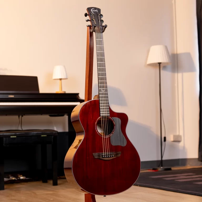 Red acoustic guitar on a stand in a living room with a piano and lamps in the background ขายราคาพิเศษ