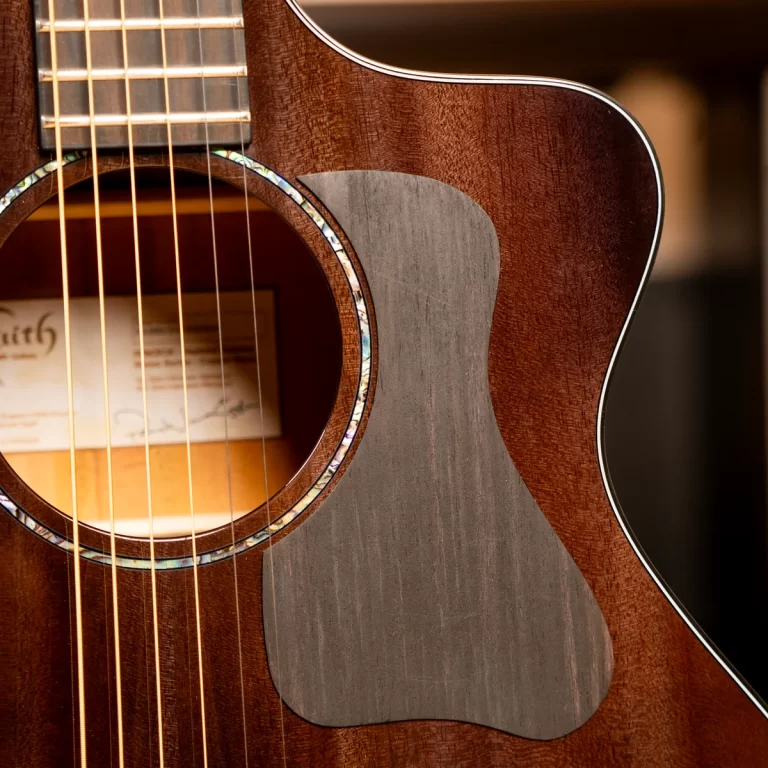 Close-up of an acoustic guitar showing the sound hole, six strings, and a grey pickguard on a warm brown body with a pearloid rosette edge. ขายราคาพิเศษ