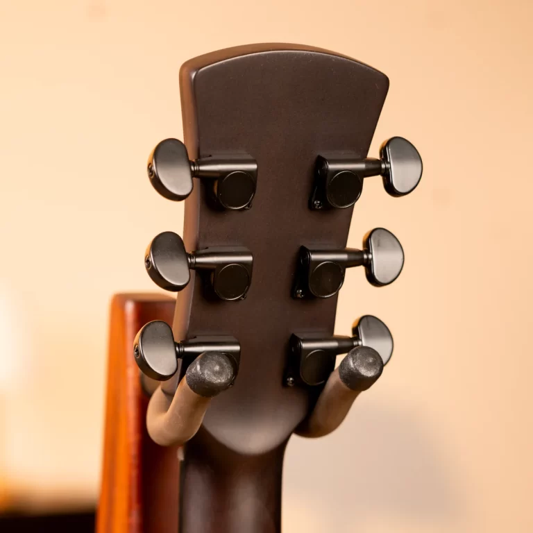 Back of a guitar headstock with six black tuning pegs against a warm beige background, viewed from behind. ขายราคาพิเศษ