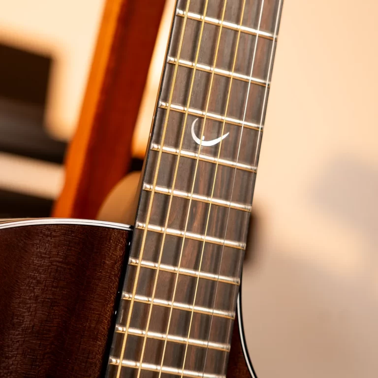 Close-up of a guitar neck and strings on a warm brown body, showing frets and a white crescent inlay on the fretboard. ขายราคาพิเศษ