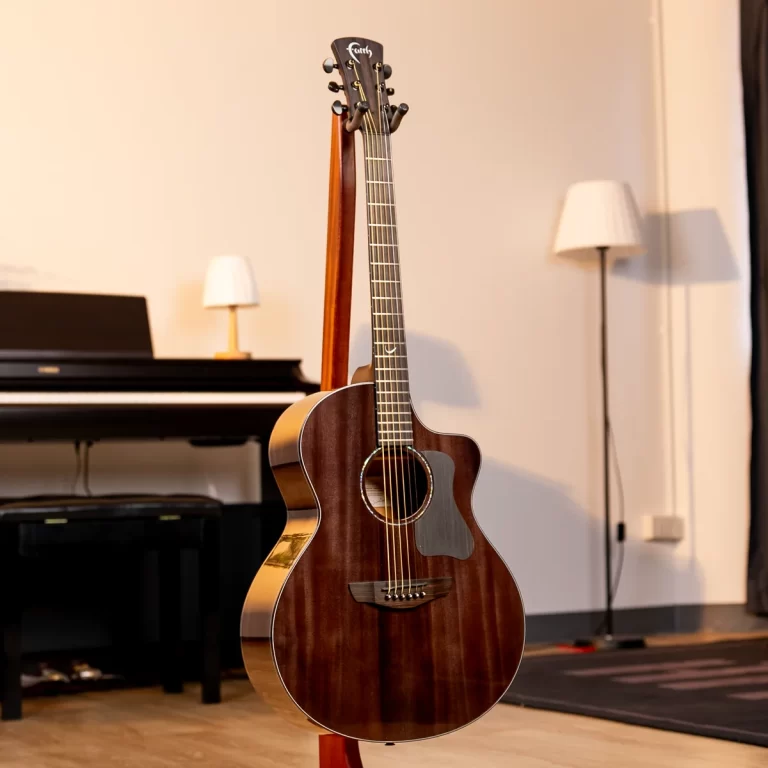 Brown acoustic guitar on a stand in a living room with a piano and lamps in the background ขายราคาพิเศษ