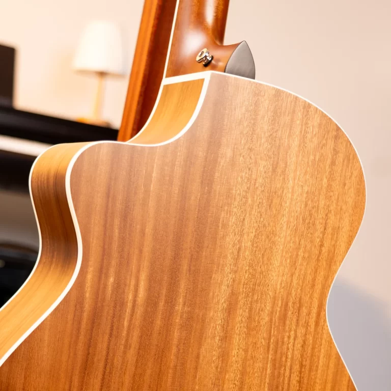Close-up of the back and side of an acoustic guitar, showing warm wood grain and white binding. ขายราคาพิเศษ