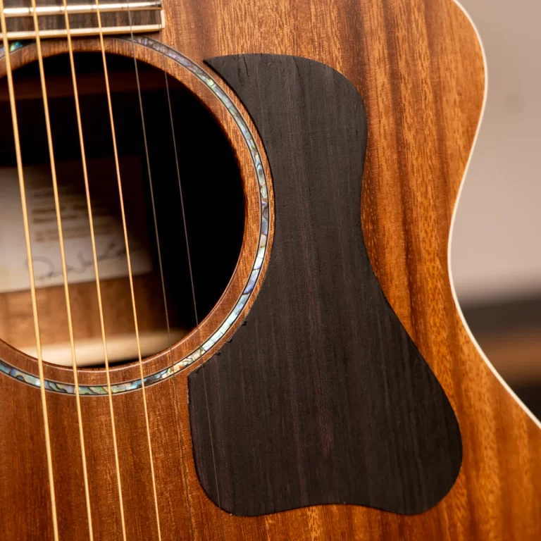 Close-up of an acoustic guitar body showing the sound hole, brown wood grain, and a dark pickguard with an iridescent rim edge nearby ขายราคาพิเศษ