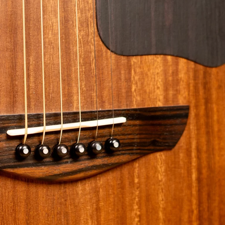 Close-up of an acoustic guitar bridge with six steel strings secured by black pins and a white saddle on a warm wood body. ขายราคาพิเศษ