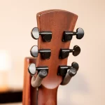 Close-up of a wooden guitar headstock with six black tuning pegs on the side, neutral background ขายราคาพิเศษ
