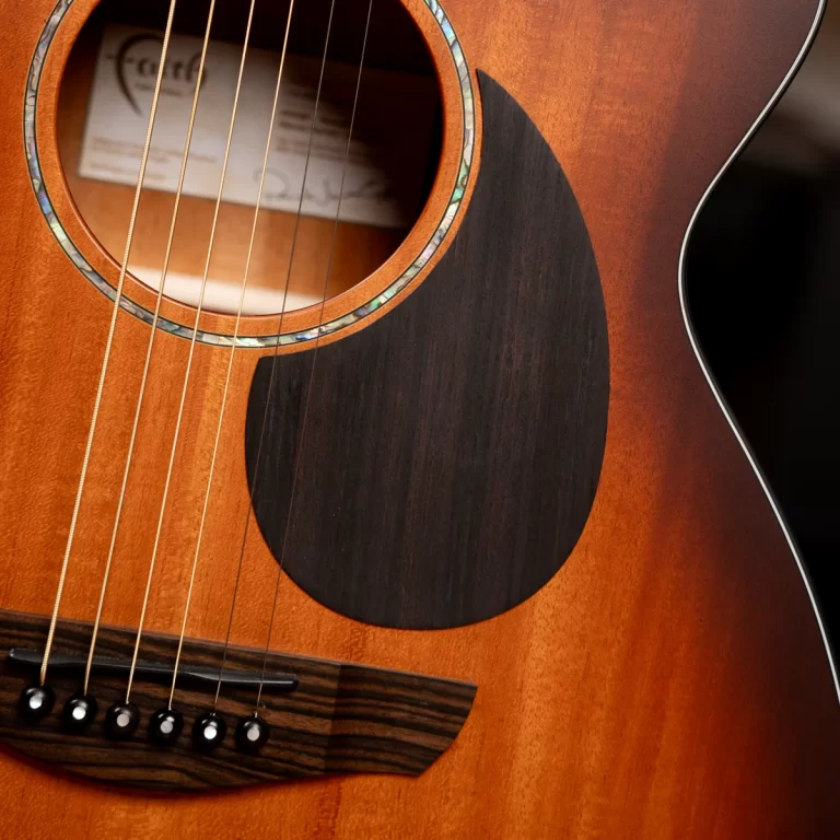 Close-up of an acoustic guitar body showing six steel strings over the bridge, soundhole rosette, and dark pickguard with a warm sunburst finish. ขายราคาพิเศษ