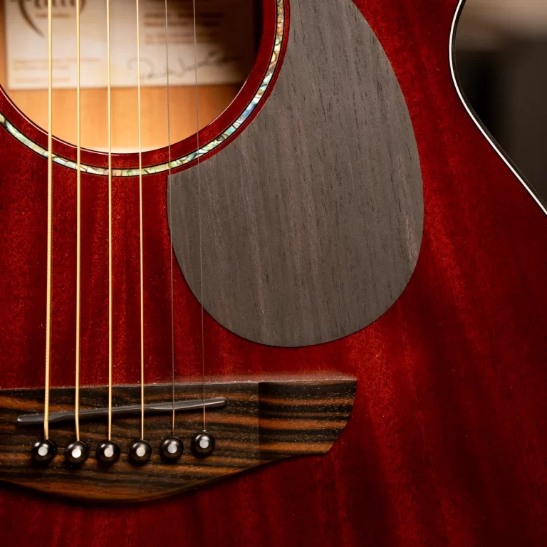 Close-up of an acoustic guitar body with strings over the bridge and a round black pickguard on a reddish wood surface. ขายราคาพิเศษ