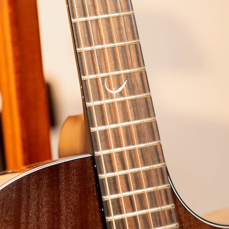 Close-up of a wooden guitar neck showing frets and a white crescent inlay on the fretboard. ขายราคาพิเศษ