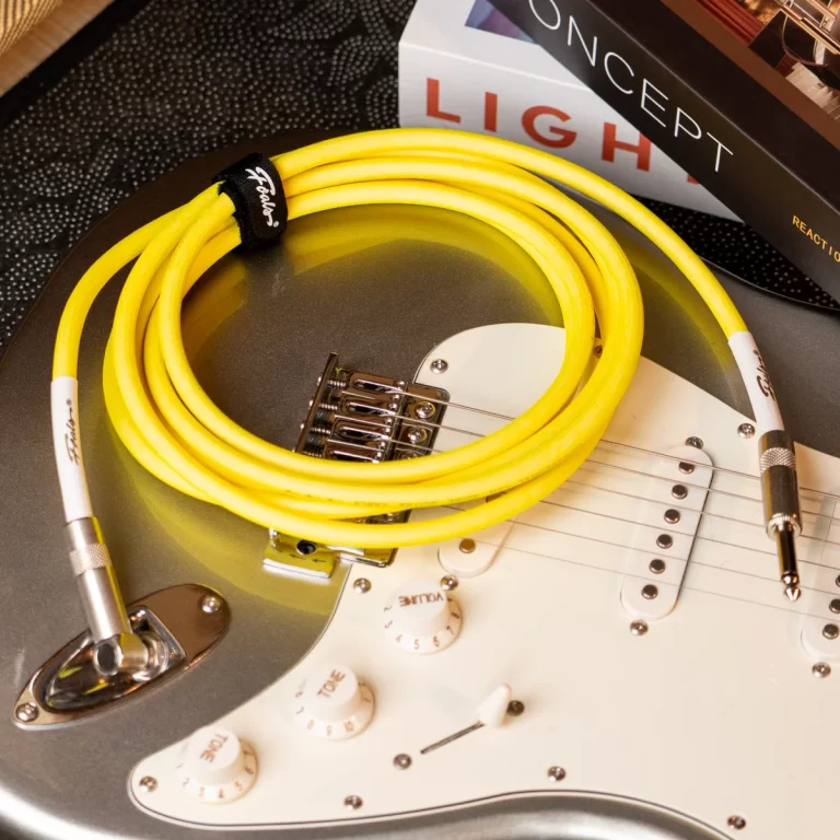 Yellow instrument cable coiled on a white Fender Stratocaster-style guitar with a silver jack plug nearby. (Informative: shows cable and guitar accessory.) ขายราคาพิเศษ