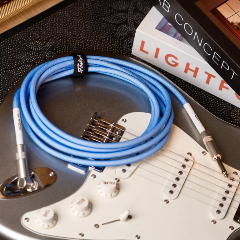 Blue coiled instrument cable resting on a silver electric guitar with white pickups and knobs. ขายราคาพิเศษ