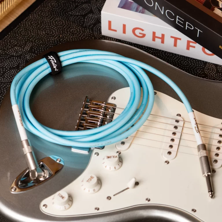 Electric guitar with a bright blue cable coiled on its body, white pickguard and knobs visible, book spines in the background labeled Concept and Lightforesight or similar. ขายราคาพิเศษ