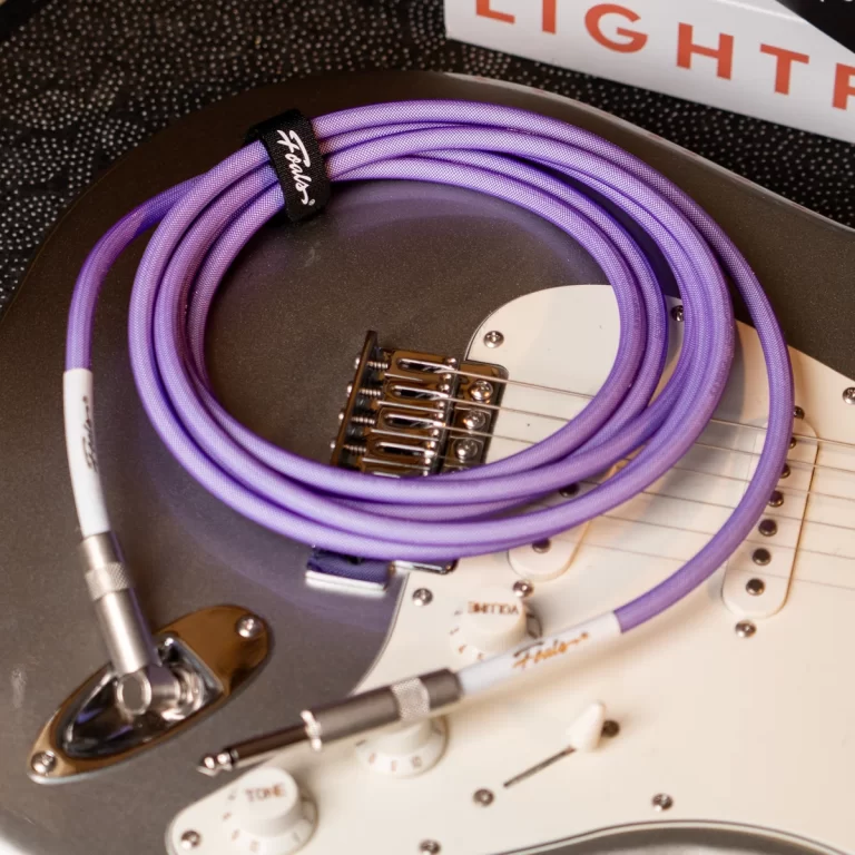 Close-up of an electric guitar with a coiled purple instrument cable resting on the pickguard area. ขายราคาพิเศษ