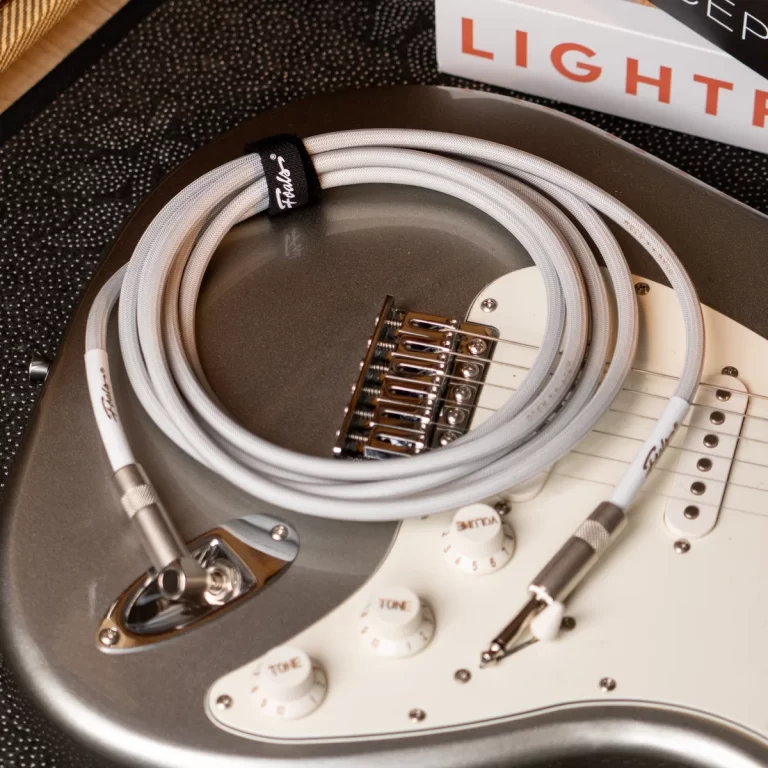 Coiled white guitar cable resting on a silver Strat-style electric guitar with control knobs and pickups visible ขายราคาพิเศษ