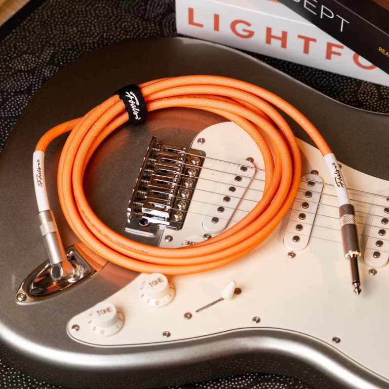 Electric guitar with a bright orange instrument cable coiled on its white pickguard and chrome hardware in the foreground. ขายราคาพิเศษ