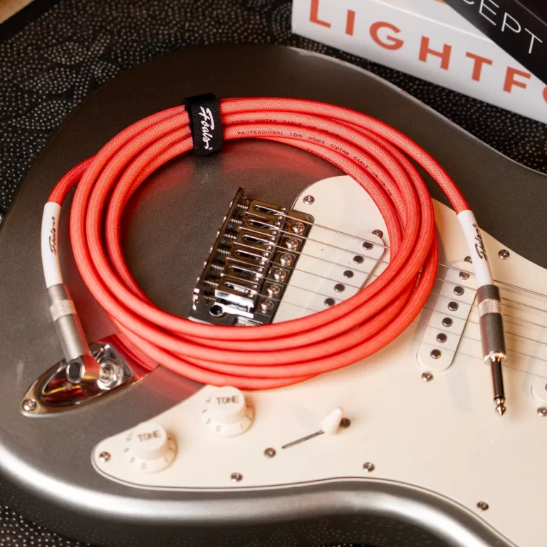 Coiled red electric guitar cable resting on a metallic gray guitar body with a white pickguard and bridge nearby. ขายราคาพิเศษ